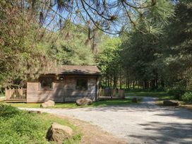 A wooden cabin with a small deck surrounded by trees on a dirt road at Sycamore Lodge in Rosliston
