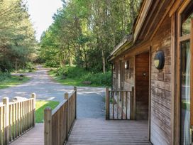 A wooden cabin porch with railings next to a gravel path and surrounded by trees at Cedar Lodge in Rosliston