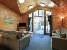 A living room with two sofas a wooden coffee table a television on a stand and large glass doors leading outside at Cedar Lodge in Rosliston
