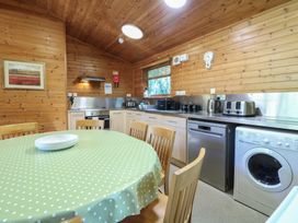 A kitchen with wooden walls a round table with a green polka dot tablecloth chairs and appliances including a washing machine and dishwasher at Cedar Lodge in Rosliston
