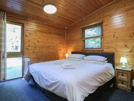 A bedroom with a double bed with white bedding wooden walls and a window at Cedar Lodge in Rosliston