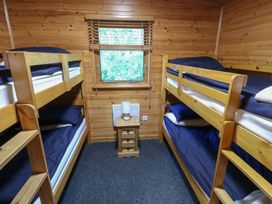 A small bedroom with two wooden bunk beds a window between them and a bedside table with a lamp at Cedar Lodge in Rosliston
