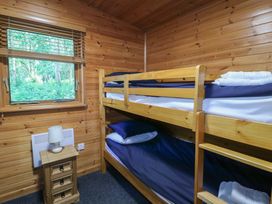 A wooden bedroom with bunk beds beside a window and a small wooden bedside table with a lamp at Cedar Lodge in Rosliston