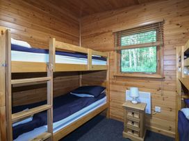 A wooden bedroom with bunk beds a small wooden nightstand and a window showing trees outside at Cedar Lodge in Rosliston