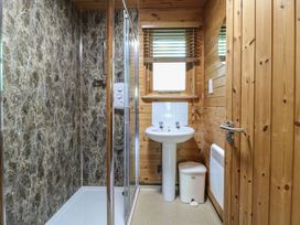 A bathroom with a shower enclosure a sink a window a bin and wooden walls at Cedar Lodge in Rosliston