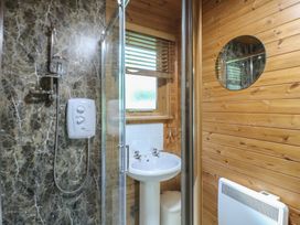 A bathroom with a shower, a white pedestal sink, a round mirror, a window with blinds, and wooden walls at Cedar Lodge in Rosliston