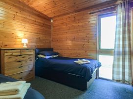 A bedroom with two single beds a wooden chest of drawers a lamp and a window with plaid curtains at Cedar Lodge in Rosliston