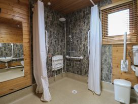 A bathroom with a walk-in shower with folding seat grab bars and a window with blinds at Cedar Lodge in Rosliston