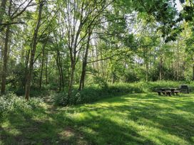A grassy clearing with trees and shrubs around a wooden picnic table and a barbecue grill at Cedar Lodge in Rosliston