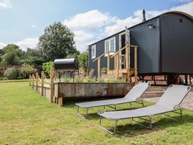 A garden with a hut, flower bed, and lounge chairs at Shepherd's Hut in Wrexham