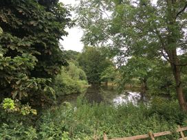 A view of trees and a pond with grass and a fence at The Garden Hut in Wrexham
