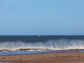 A beach with waves and a boat in the distance at Beachside Cottage Sandsend