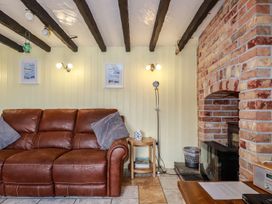 A living room with a brown leather sofa a brick fireplace and wooden beams on the ceiling at Rock Cottage in Portmellon near Mevagissey