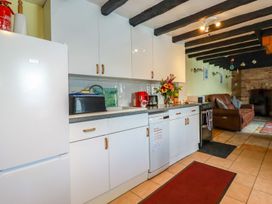 A kitchen with white cabinets and appliances next to a living area with a brown sofa and brick fireplace at Rock Cottage in Portmellon near Mevagissey