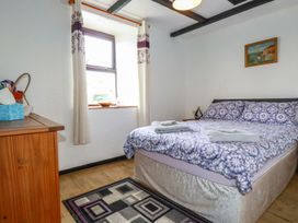 A bedroom with a double bed with patterned bedding a wooden dresser a window with curtains and a small rug on the floor at Rock Cottage Portmellon near Mevagissey
