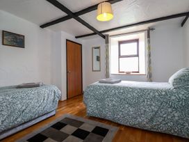 A bedroom with two single beds with patterned bedspreads a wooden door a window with curtains and a mirror on the wall at Rock Cottage Portmellon near Mevagissey