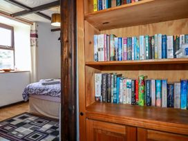 A bedroom with a bed covered in patterned bedding and folded towels beside a wooden bookshelf filled with books at Rock Cottage in Portmellon near Mevagissey