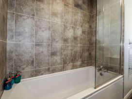 A bathtub with a glass shower screen and three soap dispensers in a bathroom at Rock Cottage in Portmellon near Mevagissey