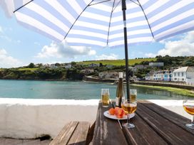 Outdoor table with wine glasses plates of fruit under a striped umbrella by the water at Rock Cottage in Portmellon near Mevagissey
