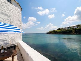 A seaside view from a balcony with a wooden table a striped blue and white umbrella and a white wall at Rock Cottage in Portmellon near Mevagissey