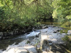 A stream flowing over rocks with trees on either side at Squirrel Cottage in Betws-Y-Coed