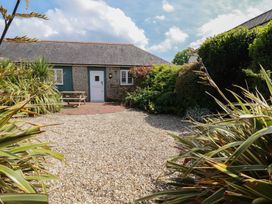 A gravel courtyard with plants and shrubs surrounding a stone building with a white door and window at The Copper House in Bodrean near Truro