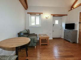 A living room with a green sofa a wooden coffee table a small round wooden dining table black chairs a wall-mounted light fixture a TV on a gray cabinet and a white door at The Copper House Bodrean near Truro