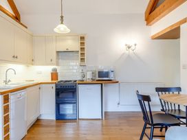 A kitchen with white cabinets wooden countertops a stove dishwasher microwave kettle and a dining table with black chairs at The Copper House in Bodrean near Truro
