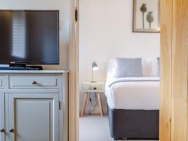 A television on a cabinet next to a bedroom with a bed bedside table and lamp at The Copper House in Bodrean near Truro