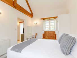 A bedroom with a bed pillows a window seat with wooden paneling a desk chair and exposed wooden ceiling beams at The Copper House Bodrean near Truro