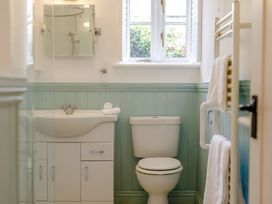 A bathroom with a white sink and cabinet, a toilet, a window with shutters, and a towel rack with towels at The Copper House in Bodrean near Truro