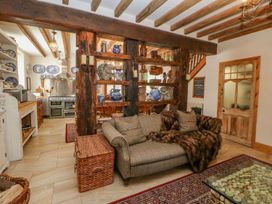A living area with a sofa, wooden shelves holding pottery and sculptures, kitchen with appliances, and a wooden door at Shaftoe Mews in Haydon Bridge