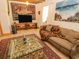 A living room with a sofa with cushions and fur throw near a coffee table with wine bottle and glasses and a TV on wooden stand at Shaftoe Mews in Haydon Bridge