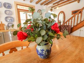 A dining area with a wooden table and vase with red flowers a wooden staircase and decorative plates on the wall at Shaftoe Mews in Haydon Bridge