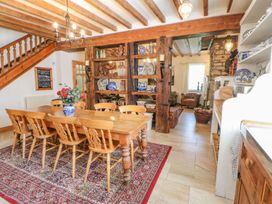 A dining room with wooden table and chairs on a rug a vase with flowers on the table wooden beams and shelves with ceramics and decorations at Shaftoe Mews in Haydon Bridge