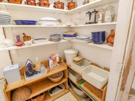 A pantry with shelves holding dishes cleaning supplies and baskets at Shaftoe Mews in Haydon Bridge