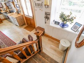 A kitchen area with wooden stairs a brown leather chair a wooden door a key holder on the wall flowers in a vase on the window sill and kitchen appliances at Shaftoe Mews in Haydon Bridge