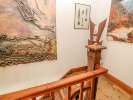 A wooden staircase with an art sculpture on the banister and abstract paintings on the walls at Shaftoe Mews in Haydon Bridge