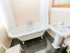 A bathroom with a bathtub a pedestal sink a white chair a mirror and a trash bin at Shaftoe Mews in Haydon Bridge
