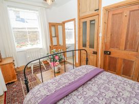 A bedroom with a metal bed frame a floral bedspread a wooden chest with a vase of flowers a wooden chair and a chest of drawers at Shaftoe Mews in Haydon Bridge