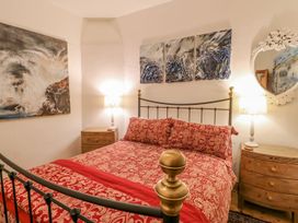 A bedroom with a bed with red patterned bedding two wooden bedside tables with lamps and three abstract paintings above the bed at Shaftoe Mews in Haydon Bridge