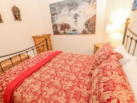A bedroom with a bed covered in red and beige patterned bedding two wooden dressers a bedside table with a lamp wall decorations including a painting and two masks at Shaftoe Mews in Haydon Bridge