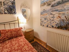 A bedroom corner with a bed covered in red floral bedding a wooden nightstand with a lamp and a white decorative mirror on the wall at Shaftoe Mews in Haydon Bridge