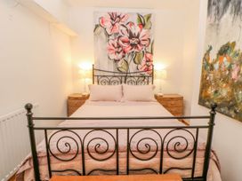 A bedroom with a black metal bed frame two bedside tables and lamps and floral paintings at Shaftoe Mews in Haydon Bridge