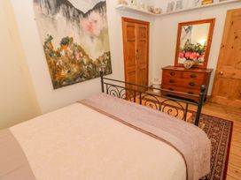 A bedroom with a bed with a metal frame a wooden dresser with a mirror and flowers a large painting and wooden doors at Shaftoe Mews in Haydon Bridge