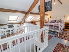 An attic bedroom with a white railing wooden beams skylight windows a bed with purple bedding and vintage furniture at Shaftoe Mews in Haydon Bridge