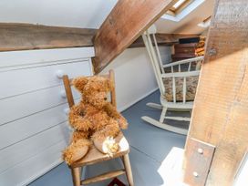 A small attic space with a wooden chair holding a teddy bear next to a white chest of drawers and a rocking chair at Shaftoe Mews in Haydon Bridge