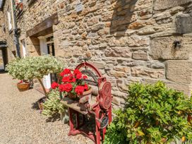 An outdoor stone wall with potted plants and a red vintage machine at Shaftoe Mews in Haydon Bridge
