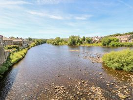 A river with stone houses and greenery on both banks at Shaftoe Mews in Haydon Bridge