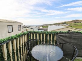 A balcony with a glass table and two black chairs overlooking caravans and hills at GM18 Clarach Bay near Aberystwyth